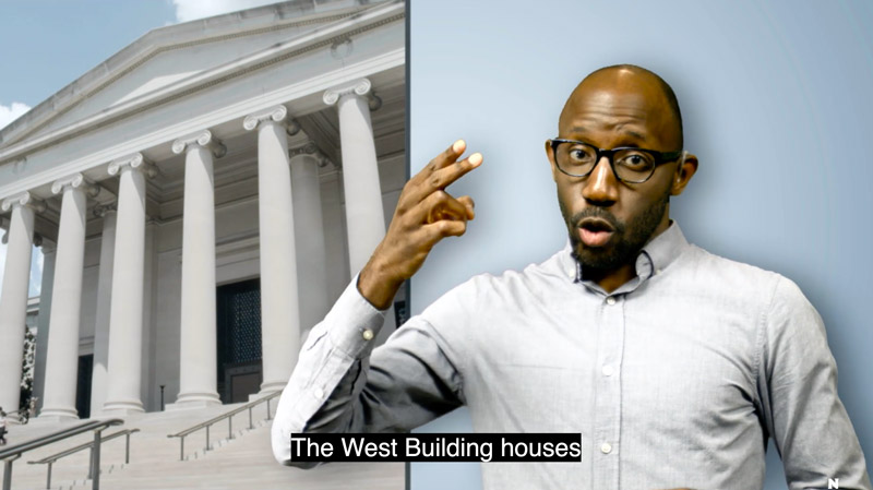 A dark skinned man with glasses and a white shirt gestures in front of a picture of the East Building. A text overlay reads 